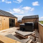 Holzterrasse mit Whirlpool, Liegen und Dusche. Blick auf grüne Landschaft.