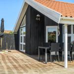 Terrasse mit Tisch, Stühlen und Sonnenschirm. Schwarze Holzwand und roter Dachziegel.
