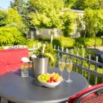 Auf der Terrasse steht ein Tisch mit Champagner, Obst und Stühlen mit roten Kissen.