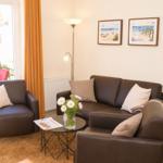 Wohnzimmer mit Sofa, Sessel und Tisch. An der Wand hängen zwei Bilder.