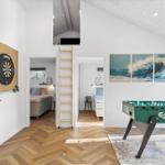 Wohnbereich mit Foosballtisch, Dartboard und Blick in Schlafzimmer. Holzfußboden und Wandbild mit Wellen.