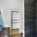 Badezimmer mit Duschbereich, Waschbecken und Toilette. Wand mit dunklen Fliesen.
