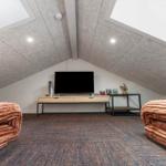 Zimmer mit Dachschrägen, TV und zwei braunen Sofas auf Teppichboden.