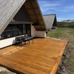 Holzterrasse mit Tisch und Stühlen vor einem A-Fachhaus mit Schiebetüren.