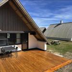 Holzterrasse mit Tisch und Stühlen vor einem A-Fachhaus mit großem Fenster.