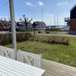 Terrasse mit weißem Tisch und Stühlen. Blick auf Hafen mit Booten und Wohnhäusern.