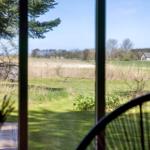 View through window to green field, trees, and a house in the distance.