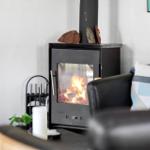 A wood-burning stove with fire, next to a sofa with cushions.