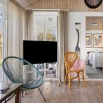 Living room with TV, chairs, and view to balcony. Bedroom visible in background.