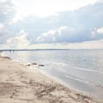 Beach with gentle waves and two people in the water under a cloudy sky.