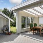 Terrasse mit Tisch und Stühlen unter Markise. Neben dem Eingang mit Pflanzen.