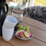 Holztisch mit Kaffeekanne, Tassen, Obst und Keksen. Hintergrund: Sitzgelegenheit mit Felldecke.