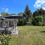 Haus mit Terrasse, Sonnenschirm und Garten. Hintergrund: Bäume und klarer Himmel.