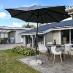 Terrasse mit Tisch, Stühlen und Sonnenschirm. Hintergrund: Haus mit Glasfront und Garten.