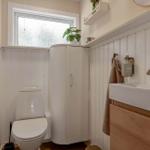 Badezimmer mit Toilette, Waschbecken und Duschabtrennung. Weiße Panele und Holzakzente.