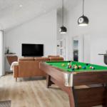 A room with a pool table, sofa, TV, and hanging lamps.