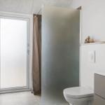 Bathroom with shower, toilet, and sink. Large door with frosted glass.