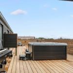Deck with hot tub, grill, and lounge chairs. Wooden deck and railings.