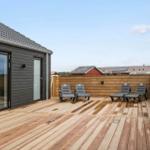 Deck with wooden planks and four lounge chairs next to a house with sliding doors.