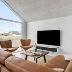 Living room with brown leather furniture, TV, and large window overlooking outdoor area.