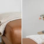 Beige blanket on brown leather sofa. Flowers in glass vase on wooden table.