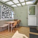 Terrasse mit Tisch, Stühlen und Fenstern. Holzboden und grüne Wände.