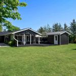 Black wooden house with terrace and green lawn under blue sky.