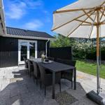 Terrace with table, chairs, and umbrella. Background: garden and house.