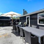 Terrace with table, chairs, and umbrella. Background: black-painted house with window.