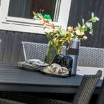 Outdoor area with table, chairs, and floral arrangement. On the table are plates, mugs, and a thermos.