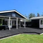 Black wooden house with terrace and garden. White windows and door. Background with trees.