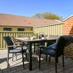 Terrasse mit Tisch, Stühlen und Teekanne. Hintergrund: Haus mit Ziegeldach und Holzgeländer.