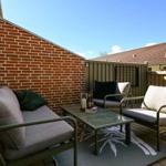 Terrasse mit Sitzgruppe, Tisch und Teppich. Hintergrund: Backsteinwand und Holzzaun.