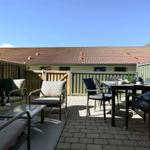 Terrasse mit Sitzgelegenheiten und Tisch. Hintergrund: Gebäude mit Ziegeldach.