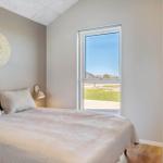 Schlafzimmer mit Bett, Wandlampe und Fensterblick auf Grünfläche.