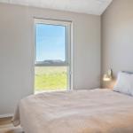 Schlafzimmer mit Bett, Fenster und Wandlampe. Draußen ist Gras und Himmel sichtbar.