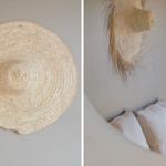 Wandgestellter Strohhut über einem Bett mit Kissen und Wandlampe.