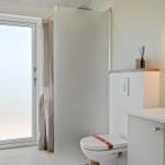 Badezimmer mit Dusche, Toilette und Waschbecken mit runden Spiegel