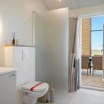 Badezimmer mit Waschbecken, Toilette und Dusche. Durchgang zur Terrasse mit Sitzgelegenheit.