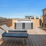 Terrasse mit Whirlpool, Liegestühlen und Holzumrandung. Blick auf moderne Häuser im Hintergrund.