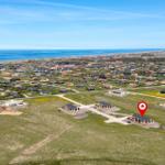 Aerial view of a coastal village with houses and a red marker on a modern building.