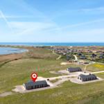 Modernes Ferienhaus auf grünem Gelände mit Blick auf Meer und Windkraftanlagen.