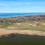 Aerial view of a coastal village with houses, a river, and wind turbines on the horizon.