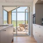 Küche mit Blick auf Terrasse und Grasland. Glastüren, Holzboden, Waschbecken, Kaffeemaschine.