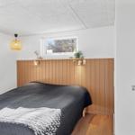 Schlafzimmer mit Bett, Holzwand und Fenster. Decke mit Paneelen, Lampe und Tür sichtbar.