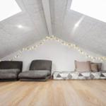 Zimmer mit Dachschrägen, zwei Sitzkissen und Matratze mit Kissen.