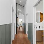 Flur mit Holzboden und grauer Paneelwand, Blick in Schlafzimmer und Badezimmer.