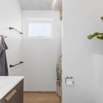 Badezimmer mit Waschbecken, Dusche und Pflanze. Fenster sorgt für Tageslicht.