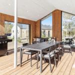 Terrasse mit Esstisch, Grill und Sitzgelegenheiten. Holzwand und große Fenster.