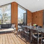 Terrasse mit Sitzgruppe, Esstisch und Grill. Holzwände und große Fenster.